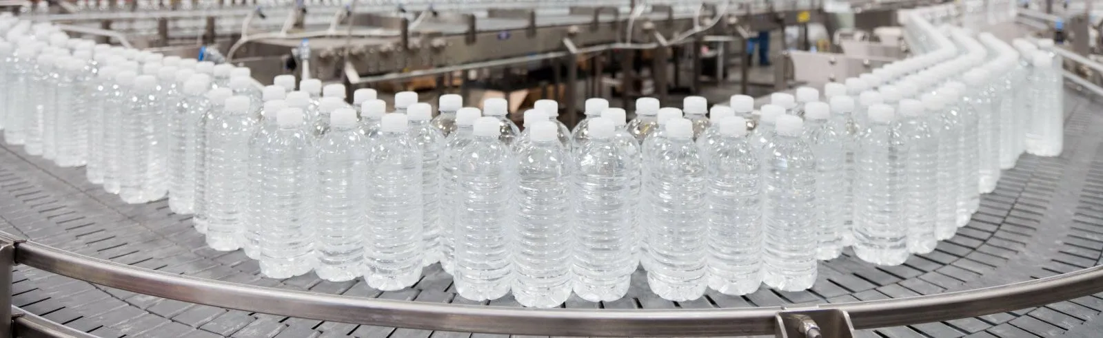 Clear bottles with white caps moving along a curved factory conveyor
